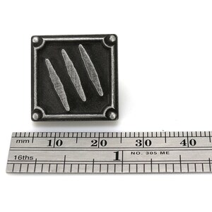 以下が含まれることがあります： 黒い背景に3本の銀色の爪痕がついた、銀色の金属製の正方形のピン。ピンの幅は約2.5cmです。