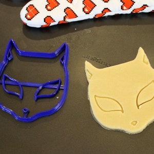 May include: A blue plastic cat cookie cutter and a cat-shaped cookie made from dough.