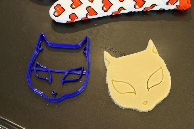 May include: A blue plastic cat cookie cutter and a cat-shaped cookie made from dough.