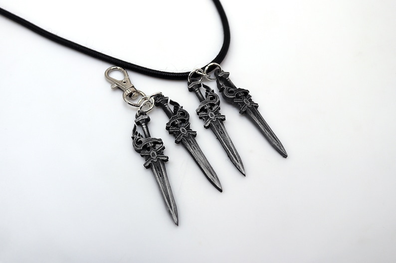 May include: A set of four silver-colored sword pendants with intricate designs, attached to a black cord and a silver clasp. The pendants are detailed with ornate handles and blades, ideal for fantasy enthusiasts.