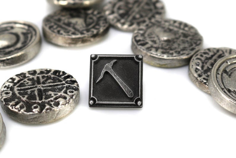 K&ouml;nnte beinhalten: Eine schwarze Metallnadel mit einem silbernen Pickel-Design. Die Nadel ist von mehreren silbernen M&uuml;nzen mit komplizierten Designs umgeben.