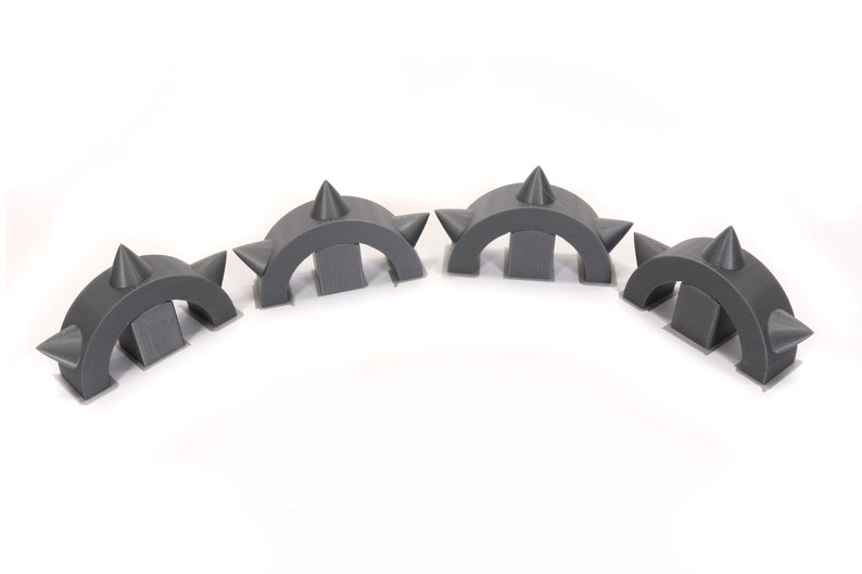 May include: Four grey plastic spiked arches, each with three spikes on top. The arches are arranged in a semi-circle.