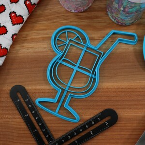 May include: Blue plastic cookie cutter shaped like a cocktail glass with a lime wedge and a straw.