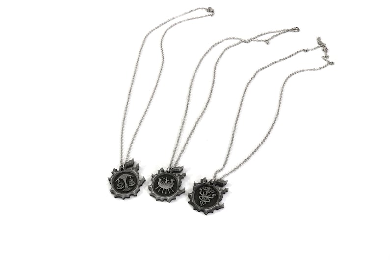 May include: Three silver necklaces with different pendants. Each pendant features a stylized design with a black finish. The pendants are shaped like a circle with a gear-like border.