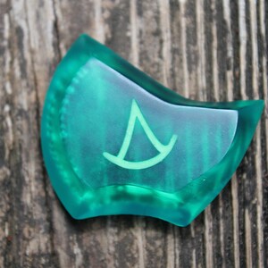 May include: A teal blue, translucent, irregularly shaped, plastic game piece with a white, stylized, triangular symbol.
