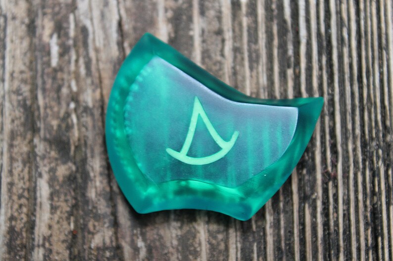 May include: A teal blue, translucent, irregularly shaped, plastic game piece with a white, stylized, triangular symbol.