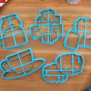 May include: A set of six blue plastic cookie cutters shaped like a teapot, sugar cubes, a tea bag, a teacup and saucer, and a loaf of bread.