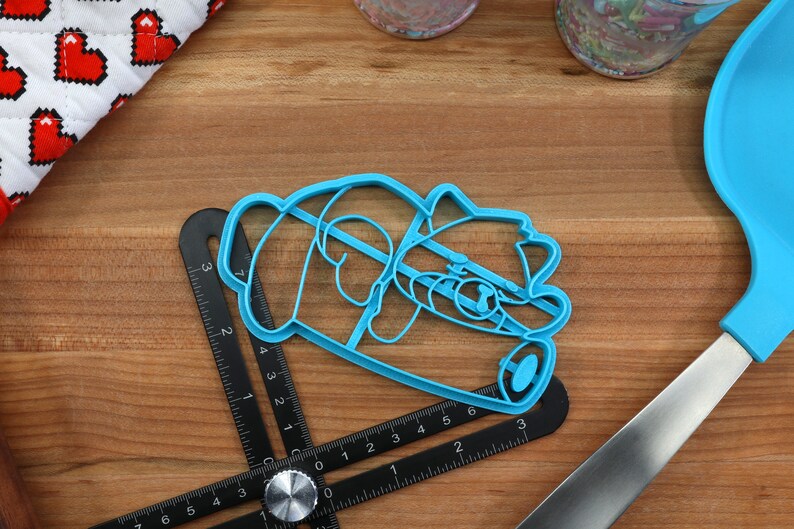May include: A blue plastic cookie cutter shaped like a panda bear. The cutter is lying on a wooden surface with a ruler and a spatula.