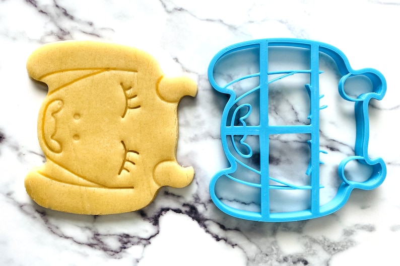 May include: A blue plastic cookie cutter shaped like a sleeping unicorn, next to a yellow sugar cookie cut with the same shape.