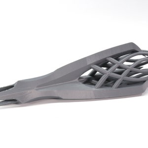 May include: A gray 3D printed object with a sharp, pointed tip and a complex, interwoven lattice structure.