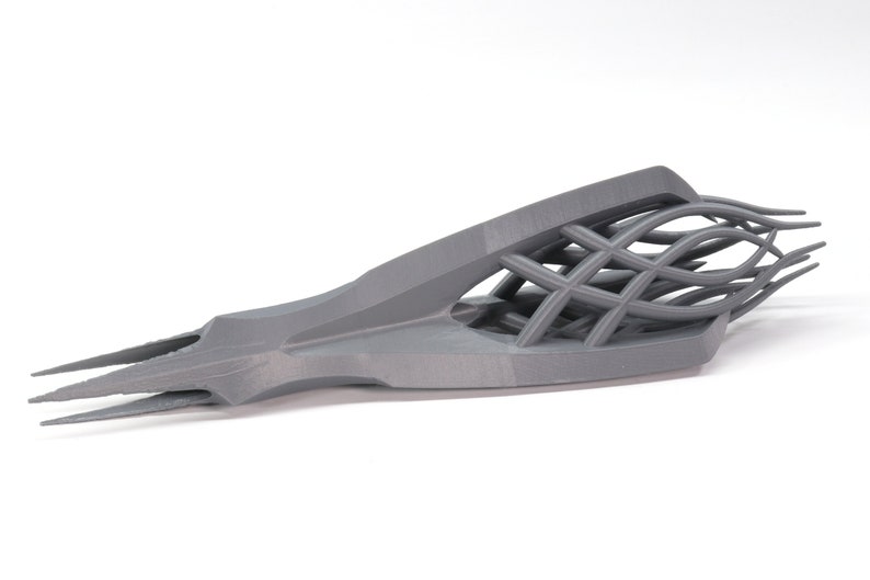 May include: A gray 3D printed object with a sharp, pointed tip and a complex, interwoven lattice structure.