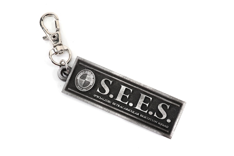May include: A silver keychain with a black rectangular tag that reads "S.E.E.S. SPECIALIZED EXTRACURRICULAR EXECUTION SQUAD".
