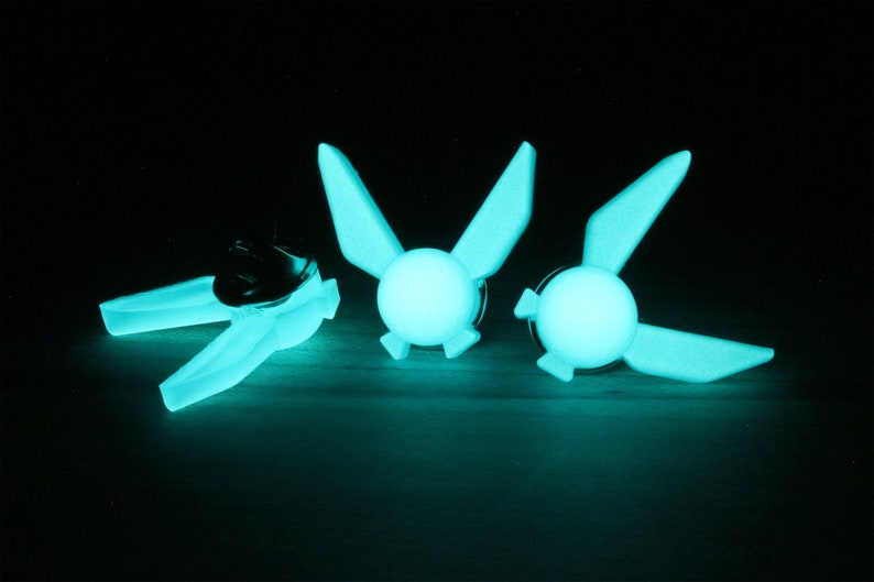 Peut inclure: Trois &eacute;pingles en plastique vert qui brillent dans le noir en forme de Triforce de la s&eacute;rie de jeux vid&eacute;o The Legend of Zelda.