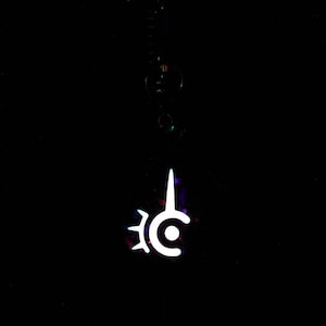 May include: A white pendant with a unique, stylized design, hanging against a black background. The pendant features a central circle with a vertical spike and a gear-like shape on the left side. The design glows brightly.