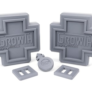 May include: Two gray plastic cross-shaped objects with the word "GROWTH" embossed on them. There are also three smaller gray plastic objects, including a round one with the letters "ADD" embossed on it.