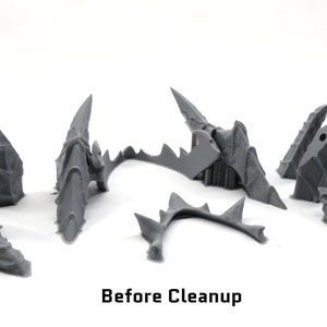 May include: A set of six grey plastic pieces, likely parts of a 3D printed model, before cleaning. The pieces are arranged on a white surface. The text "Before Cleanup" is visible below the pieces.