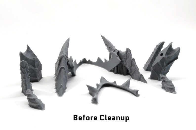 May include: A set of six grey plastic pieces, likely parts of a 3D printed model, before cleaning. The pieces are arranged on a white surface. The text "Before Cleanup" is visible below the pieces.