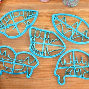 May include: Five blue plastic cookie cutters shaped like different types of mouths with teeth, fangs, and lips.