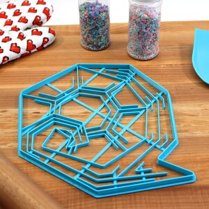 May include: A blue plastic snowflake cookie cutter on a wooden surface with a rolling pin, oven mitts, and two jars of sprinkles.