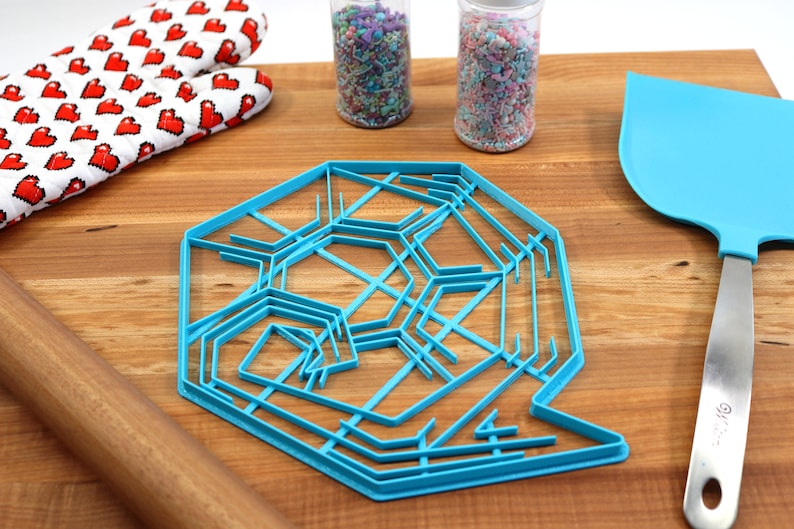 May include: A blue plastic snowflake cookie cutter on a wooden surface with a rolling pin, oven mitts, and two jars of sprinkles.
