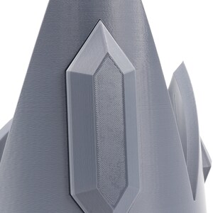 May include: A gray, 3D printed crown with a pointed, crystal-like design on the top.