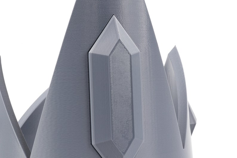 May include: A gray, 3D printed crown with a pointed, crystal-like design on the top.