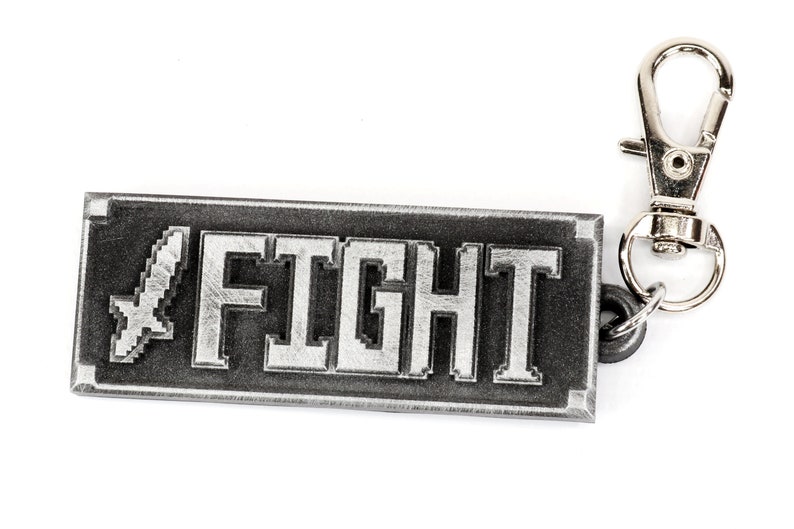May include: A silver metal keychain with a black rectangular tag that says "FIGHT" in white pixelated letters. A silver sword icon is to the left of the text. The keychain has a silver swivel clasp.