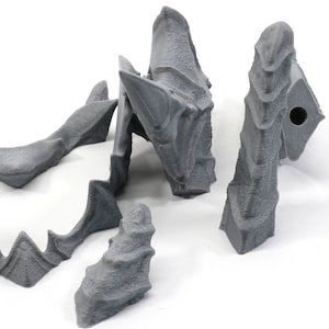 May include: Five grey 3D printed pieces of a dragon sculpture. The pieces are made of a textured plastic and have a rough, organic look.