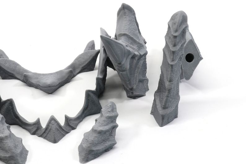 May include: Five grey 3D printed pieces of a dragon sculpture. The pieces are made of a textured plastic and have a rough, organic look.