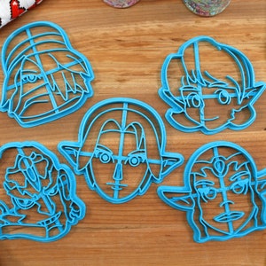 May include: Set of five blue plastic cookie cutters shaped like cartoon characters with elf ears. The cutters are on a wooden surface.