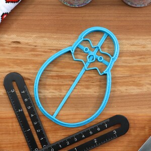 May include: A blue plastic cookie cutter shaped like a penguin. The cutter is on a wooden surface.