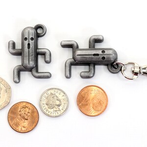 May include: Two silver metal keychain charms shaped like a video game character. The charms are attached to a silver metal key ring. There are four coins in the image, two silver and two copper.