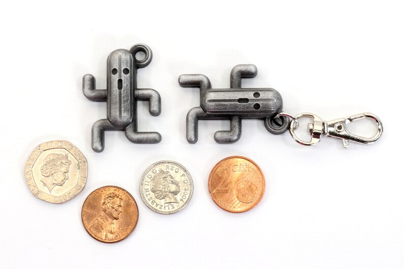 May include: Two silver metal keychain charms shaped like a video game character. The charms are attached to a silver metal key ring. There are four coins in the image, two silver and two copper.