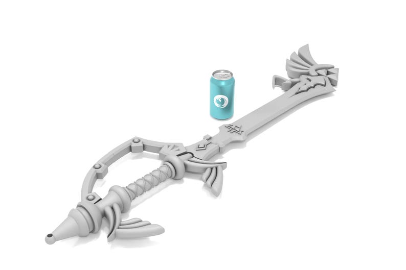 K&ouml;nnte beinhalten: Eine wei&szlig;e Plastik-Replik der Kingdom Key, ein schl&uuml;sself&ouml;rmiges Schwert aus der Kingdom Hearts-Videospielserie. Das Schwert liegt auf einer wei&szlig;en Oberfl&auml;che neben einer blauen Dose.