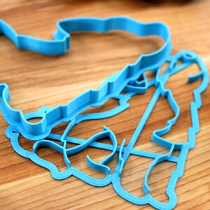 May include: Two blue plastic cookie cutters, one shaped like a heart and the other shaped like a person, are lying on a wooden surface.