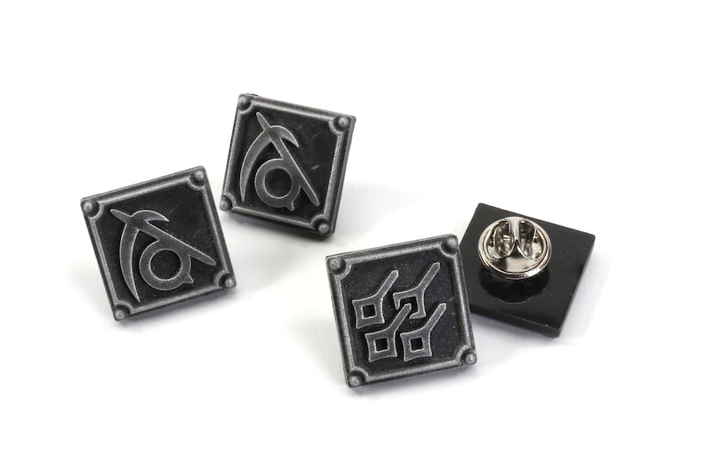 May include: Three silver metal pins with different designs. The first pin features a stylized symbol with a crescent moon and a circle. The second pin features a stylized symbol with a crescent moon and a circle. The third pin features a stylized symbol with four squares.