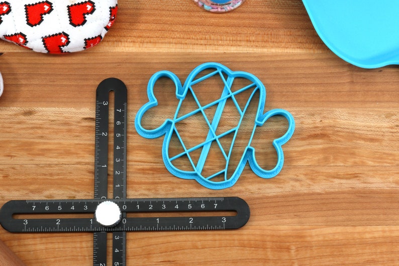 Puede incluir: Un cortador de galletas de pl&aacute;stico azul en forma de coraz&oacute;n con un dise&ntilde;o de celos&iacute;a en el interior. El cortador est&aacute; sobre una superficie de madera.