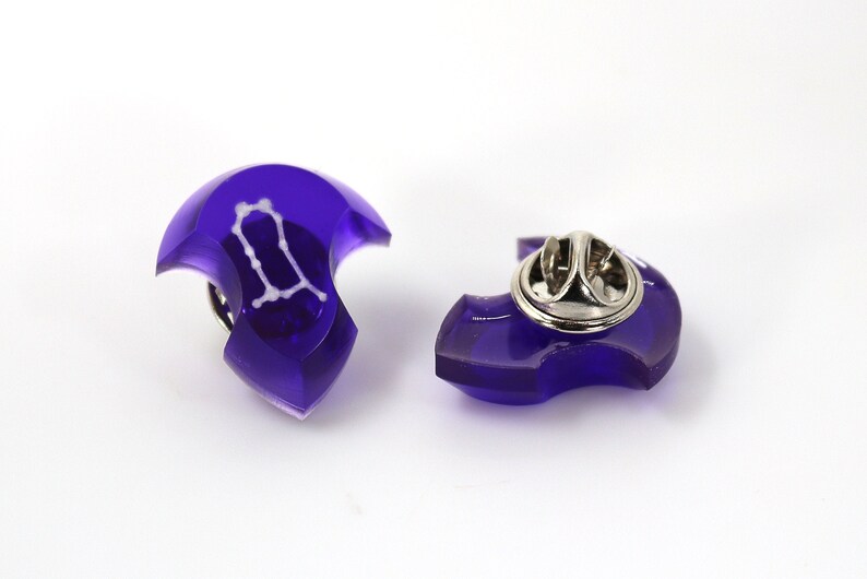 May include: Purple Gemini zodiac sign pin with a silver pin back.