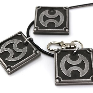 May include: Three silver-toned pendants with a black and silver symbol. The pendants are on a black cord necklace and a silver key chain.