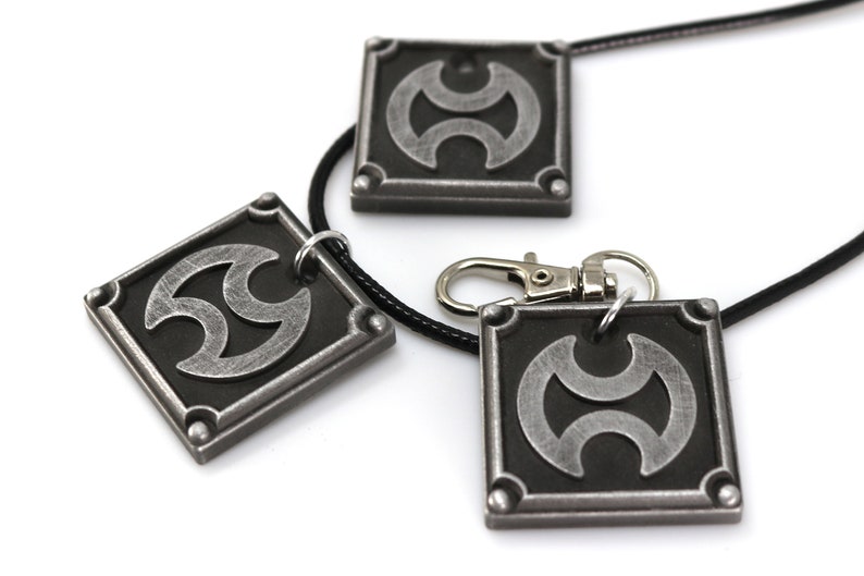 May include: Three silver-toned pendants with a black and silver symbol. The pendants are on a black cord necklace and a silver key chain.