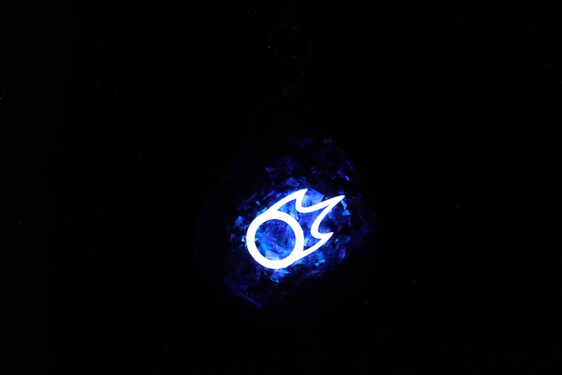 Puede incluir: Una bola de cristal azul con un s&iacute;mbolo de llama blanca brillante en su interior. El s&iacute;mbolo es un c&iacute;rculo con una llama que sale de la parte superior.