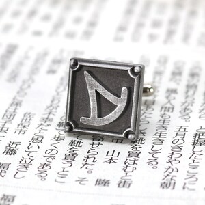 May include: Silver cufflinks with a square design featuring a stylized letter "Y" in the center.