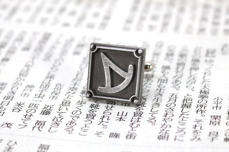 May include: Silver cufflinks with a square design featuring a stylized letter "Y" in the center.
