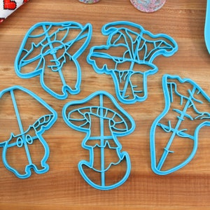 May include: Five blue plastic mushroom-shaped cookie cutters on a wooden surface.