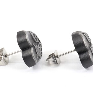 May include: A pair of black heart-shaped stud earrings with a detailed design. The earrings have silver posts and backs.