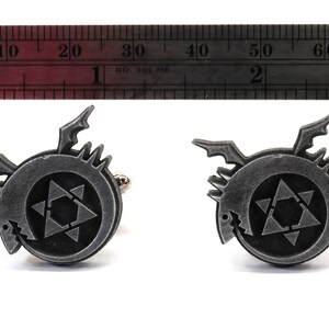 May include: A pair of silver cufflinks featuring a black and white symbol with a star and a dragon. The cufflinks are approximately 1.5 inches in diameter.