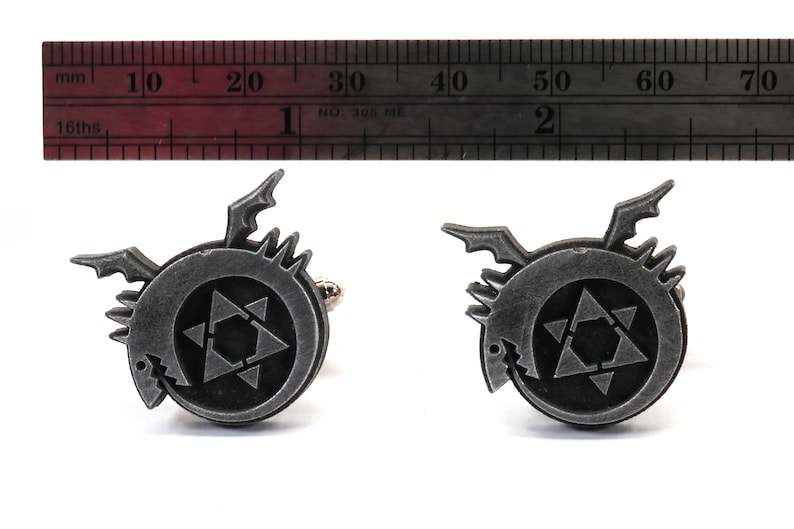 May include: A pair of silver cufflinks featuring a black and white symbol with a star and a dragon. The cufflinks are approximately 1.5 inches in diameter.