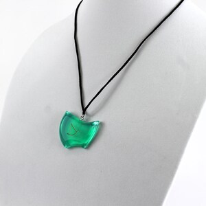 May include: A green pendant necklace with a gold symbol on a black cord. The pendant is shaped like a crescent moon.