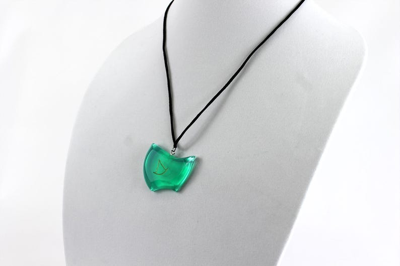 May include: A green pendant necklace with a gold symbol on a black cord. The pendant is shaped like a crescent moon.