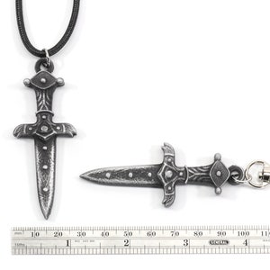 May include: A silver-toned dagger pendant with a black cord necklace and a matching silver-toned dagger keychain. The dagger has a detailed design with a pointed tip and a rounded handle. The pendant is approximately 7 cm long and the keychain is approximately 6 cm long.